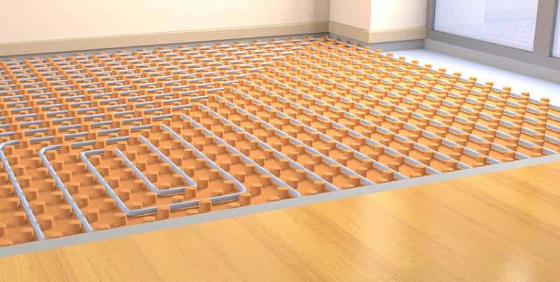 Installation d'un système de chauffage au sol avec des tuyaux gris sur des panneaux isolants oranges, avant la pose du parquet en bois clair.