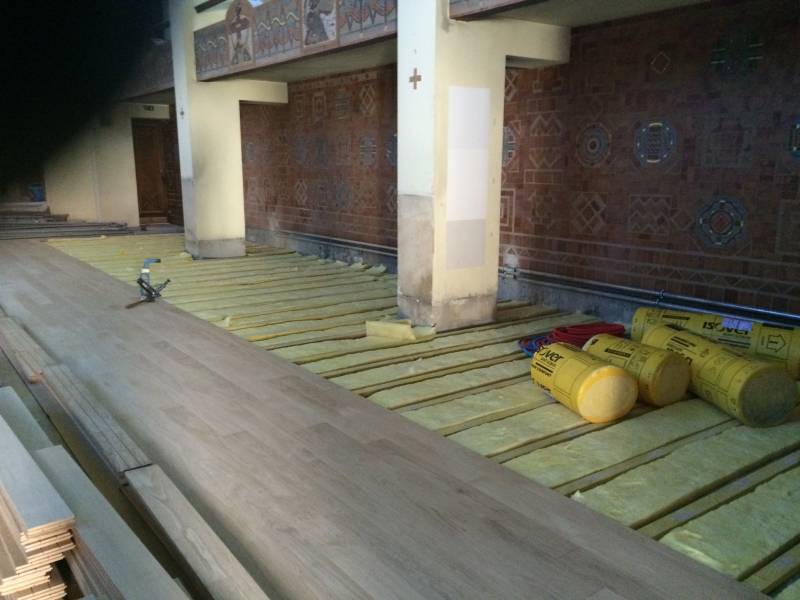 Installation d'un parquet flottant sur isolation Isover. Lattes de bois et rouleaux d'isolant au sol dans une grande salle en rénovation.