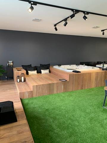 Intérieur design avec jacuzzi encastré sur plateforme en bois. Coin salon, sol gazon synthétique vert. Éclairage moderne au plafond.