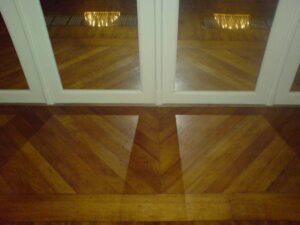 Sol en parquet chevron bois clair avec reflets de chandelier et portes blanches. Design intérieur élégant et brillant.