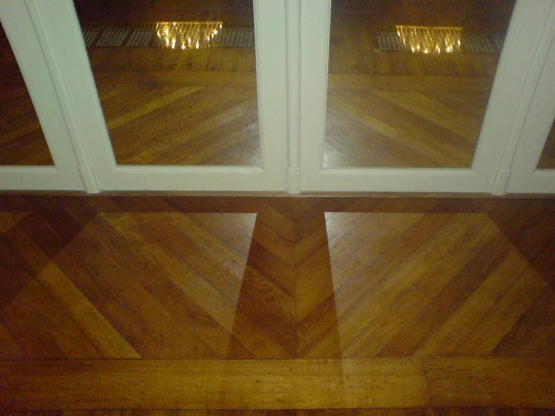 Sol en parquet chevron bois clair avec reflets de chandelier et portes blanches. Design intérieur élégant et brillant.