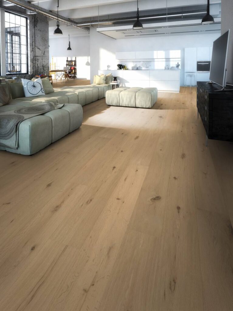 Sol parquet bois clair dans grand salon moderne ouvert avec canapé modulaire vert pâle et cuisine blanche.