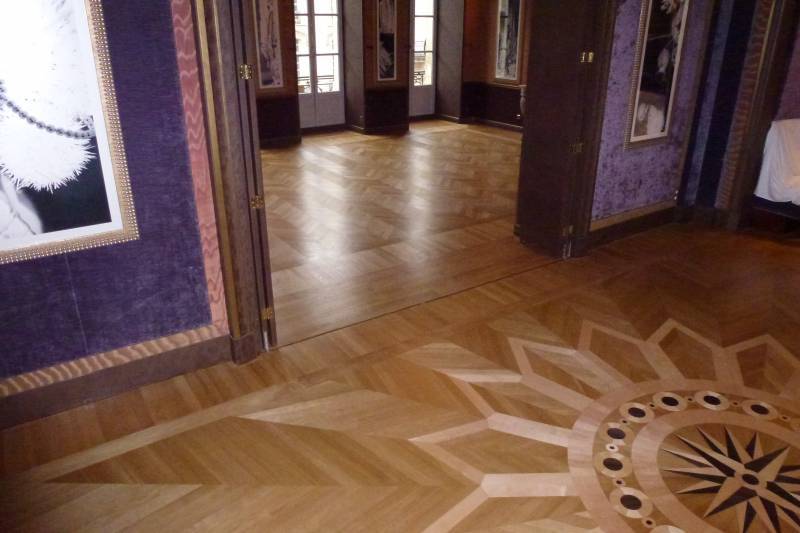 Sols en parquet de bois luxueux avec motif géométrique complexe et rose des vents, murs pourpres ornés de cadres. Un intérieur élégant.