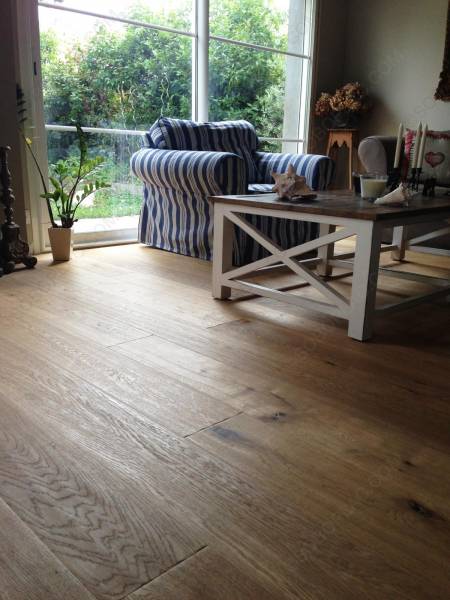 Salon lumineux avec parquet en bois clair, fauteuil rayé bleu et blanc, table basse et grande fenêtre sur jardin.