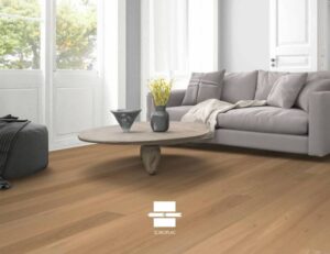 Parquet bois clair SOBOPLAC dans salon moderne, canapé gris et fenêtre lumineuse.