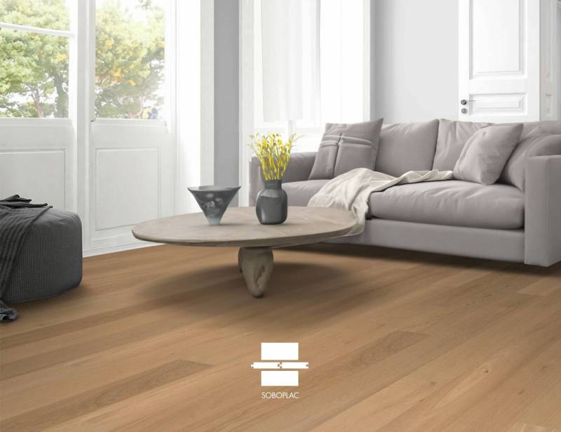 Parquet bois clair SOBOPLAC dans salon moderne, canapé gris et fenêtre lumineuse.