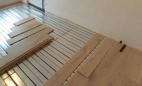 Installation de parquet en bois clair sur un système de chauffage au sol moderne, visible avec ses tuyaux quadrillés lors d'une rénovation.