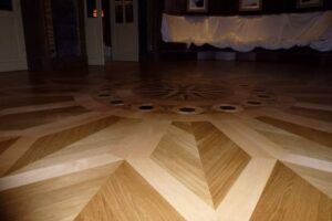 Élégant parquet en bois poli avec marqueterie complexe : rosace centrale, motifs géométriques et incrustations sombres. Lumière tamisée.