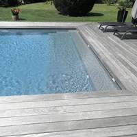 Piscine rectangulaire moderne à eau bleue, margelle et plage en bois grisé. Escalier intégré, transats sur terrasse ensoleillée.