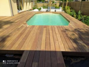 Aménagement extérieur moderne avec piscine rectangulaire turquoise et grande terrasse en bois clair. Jardin verdoyant. REDMI NOTE 8 AI QUAD CAMERA.