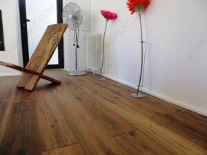 Plancher en bois large et chaleureux avec chaise africaine sculptée, ventilateur, radiateur et fleurs décoratives.