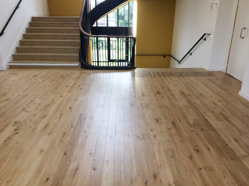 Sol en parquet clair d'un hall moderne avec grand escalier en colimaçon à rampe noire, mur jaune moutarde et signalisation tactile.