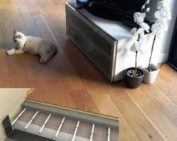 Chat beige sur plancher en bois clair, près d'un meuble TV. En bas, installation de chauffage au sol sous parquet flottant.