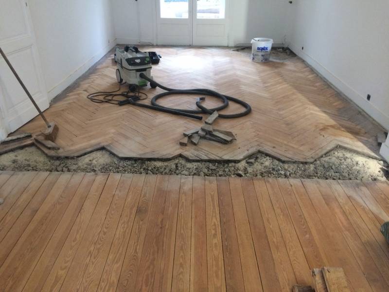 Rénovation de parquet chevrons et planches de bois. Ponceuse Festool et aspirateur au sol, une zone de parquet est retirée pour réparation.