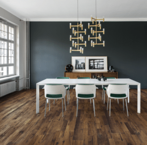 Salle à manger moderne avec grande table blanche, chaises design vertes, parquet rustique, buffet en bois et lustre doré sculptural.