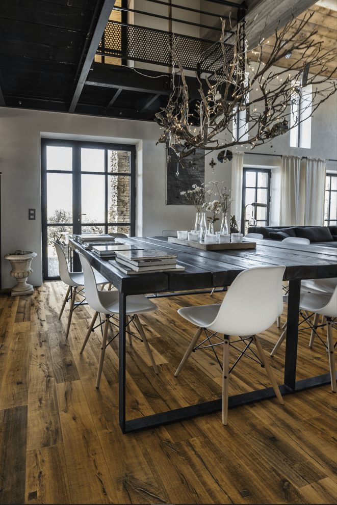 Salle à manger industrielle loft, grande table en bois, chaises modernes, lustre branches, parquet chêne, lumière naturelle.