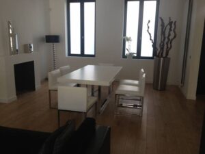 Salle à manger moderne et lumineuse avec table blanche, chaises design, cheminée et lampadaire. Plancher en bois clair.