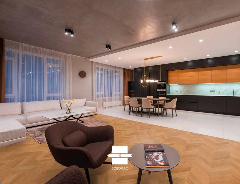 Salon, salle à manger et cuisine ouverts avec parquet chevrons SOBOPLAC. Canapé blanc, fauteuil marron. Cuisine moderne.