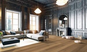 Salon luxueux avec murs à panneaux sombres, cheminée, grand canapé sectionnel gris et parquet en bois clair.