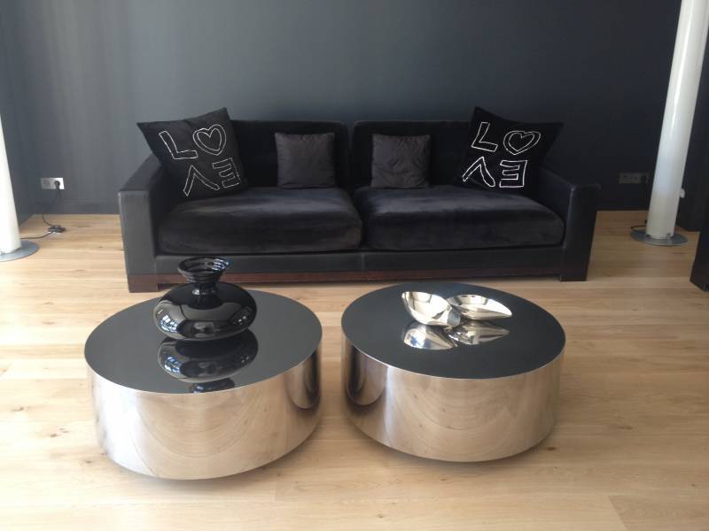 Salon moderne: canapé noir avec coussins "LOVE", deux tables basses rondes argentées et décoration chic sur parquet clair.