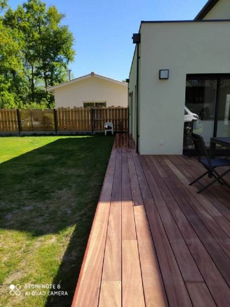 Large terrasse en bois devant une maison moderne, pelouse verte. Clôture et maison en arrière-plan. (REDMI NOTE 8 AI QUAD CAMERA)