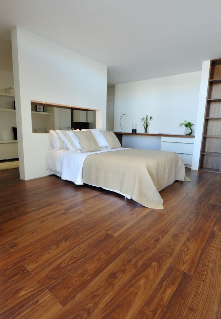 Chambre moderne avec lit double beige, plancher bois foncé. Mur-tête de lit intégré lumineux, bureau minimaliste et bibliothèque bois.