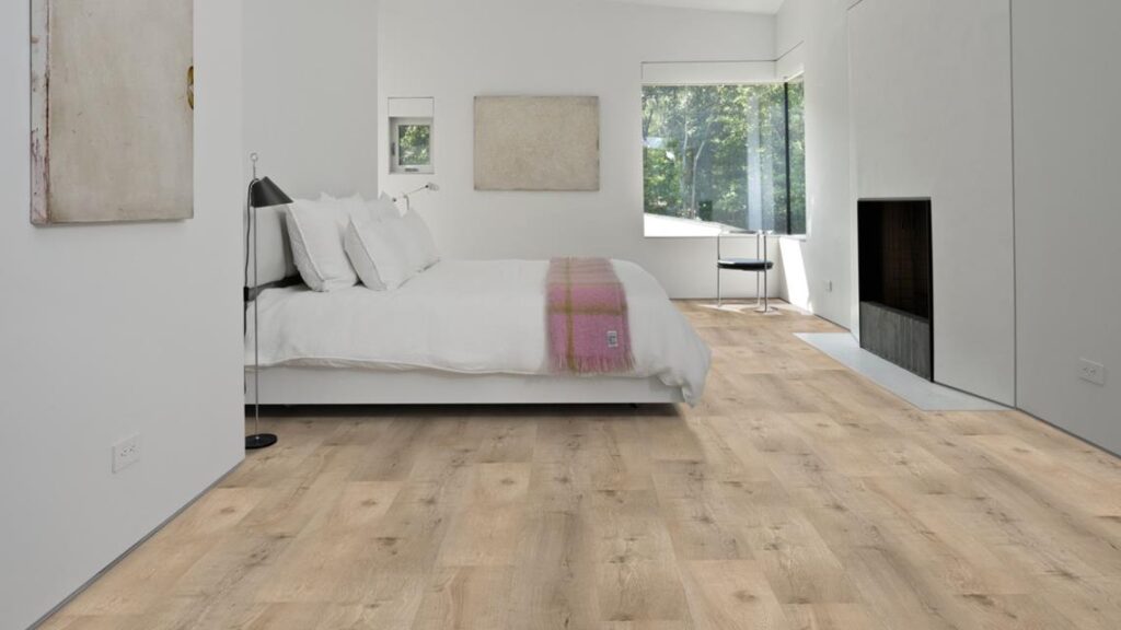 Chambre moderne lumineuse. Parquet en chêne clair à planches larges. Lit blanc, jeté rose et foyer encastré dans un mur blanc minimaliste.