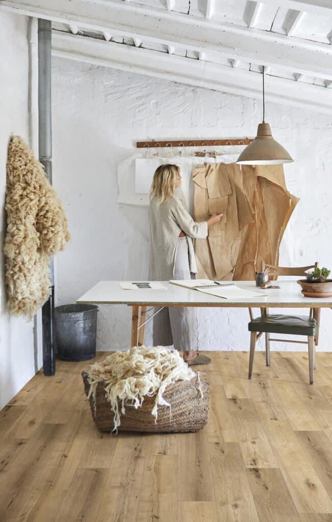 Designer ajustant des patrons en papier sur un mur blanc texturé dans un studio artisanal. Laine brute sur un parquet chêne clair.