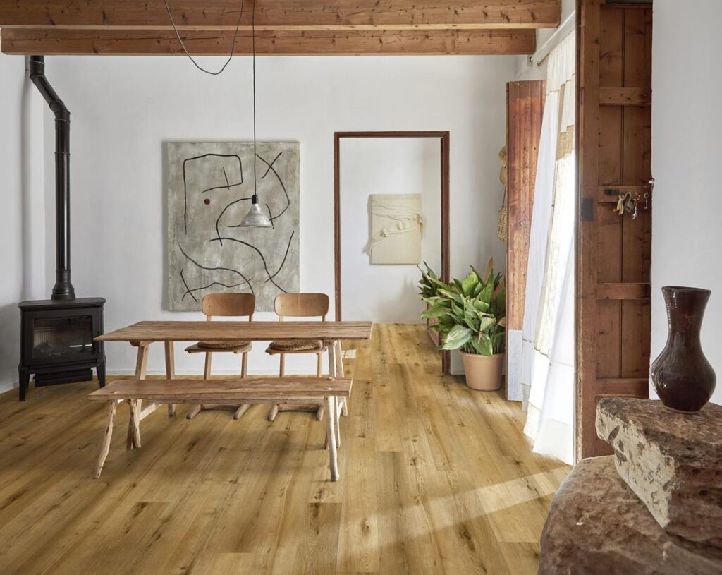 Intérieur rustique: sol bois clair, poutres apparentes, table et bancs en bois brut, poêle à bois, art abstrait.